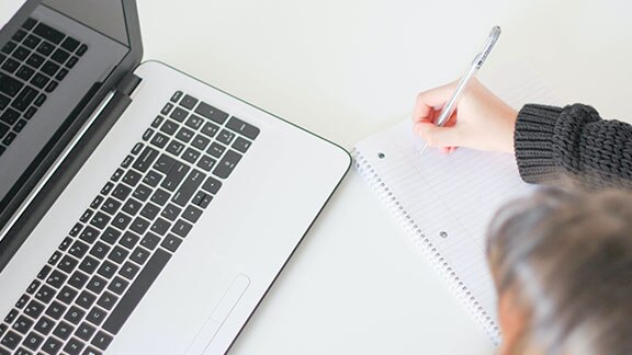 Women writing on desk with laptop